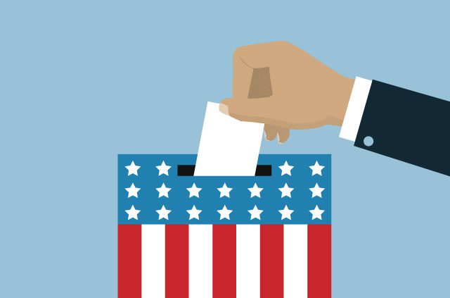 Hand putting a ballot in a box with the U.S. flag on it.